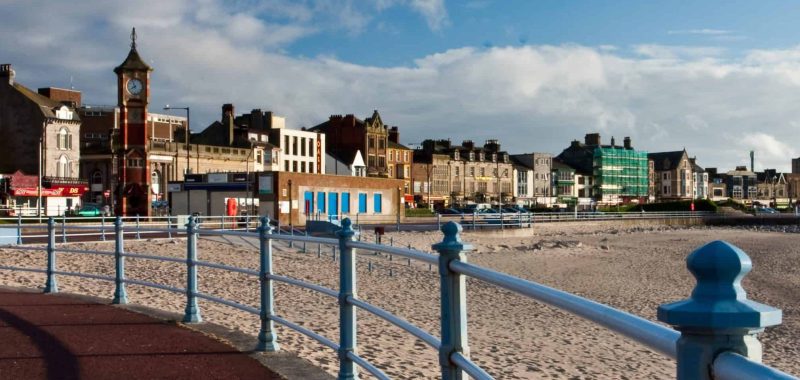 A photo on a sunny day from the Prom looking towards the clocktower and Winter Gardens across a stretch of sandy beach.